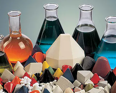 Plastic and ceramic finishing media in front of laboratory flasks of compounds